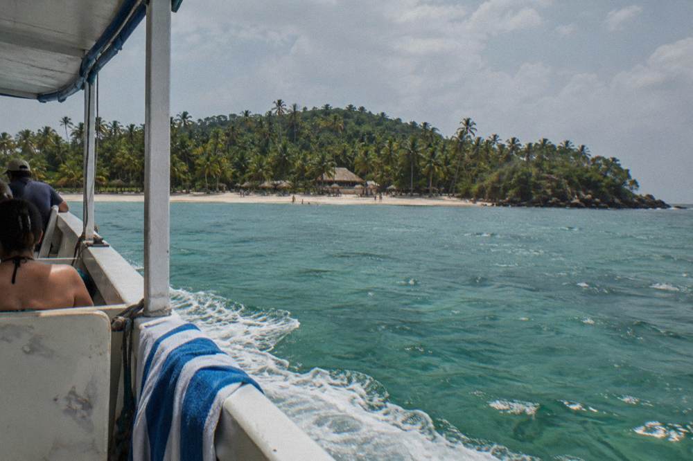 Tour boat crossing open turquoise water toward a palm covered island beach